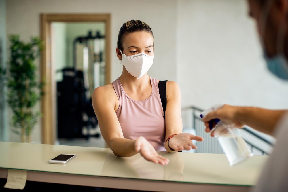 Athletic woman with face mask getting her hands disinfected at health club