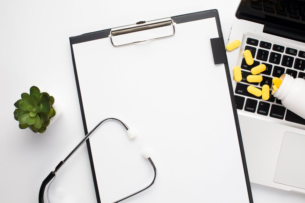 Clipboard with white paper near pills spilling out on laptop and stethoscope over desk